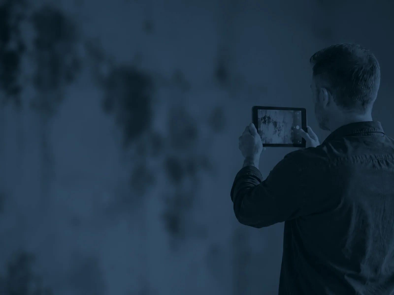 Inspector photographing black mould on a wall with a tablet during an HHSRS assessment